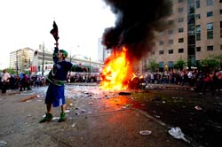 rioter in hockey gear in front of a car fire