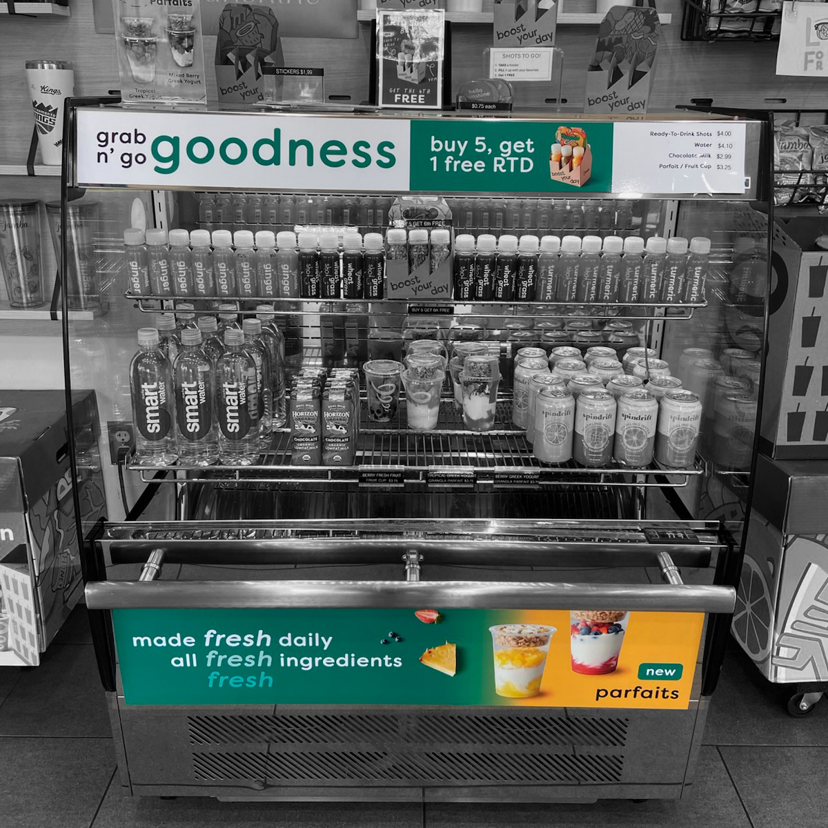 A refrigerator with advertisements that read 'Grab n Go Goodness', 'Buy 5, get 1 free RTD (Ready-To-Drink), and 'Made Fresh Daily, All Fresh Ingredients - New Parfaits'.