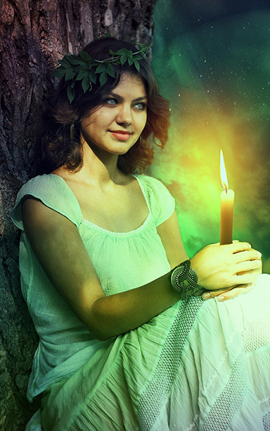A celtic woman in a white dress in the woods holding a lit candle.