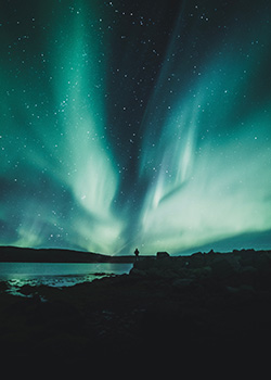 Blue Northern lights with silhoutte of man against water