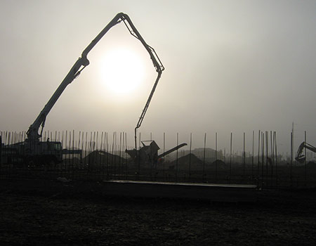 An image of a silhoutte of a boom pump manuevering to pour a foundation as the sunsets in Napa, Ca