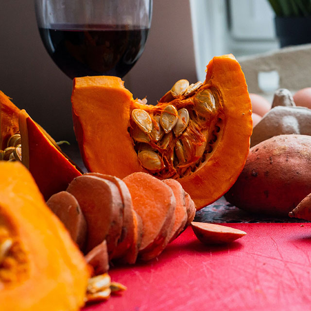 A slice of sweet potato next to a glass of wine and slice of pumpkin.