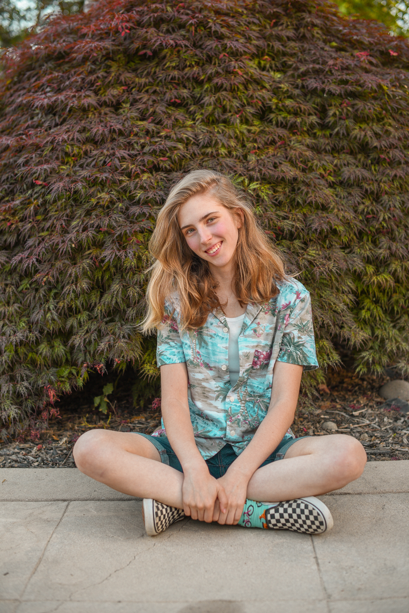 Teagan sitting in front of a Japanese maple tree, smiling at the camera.