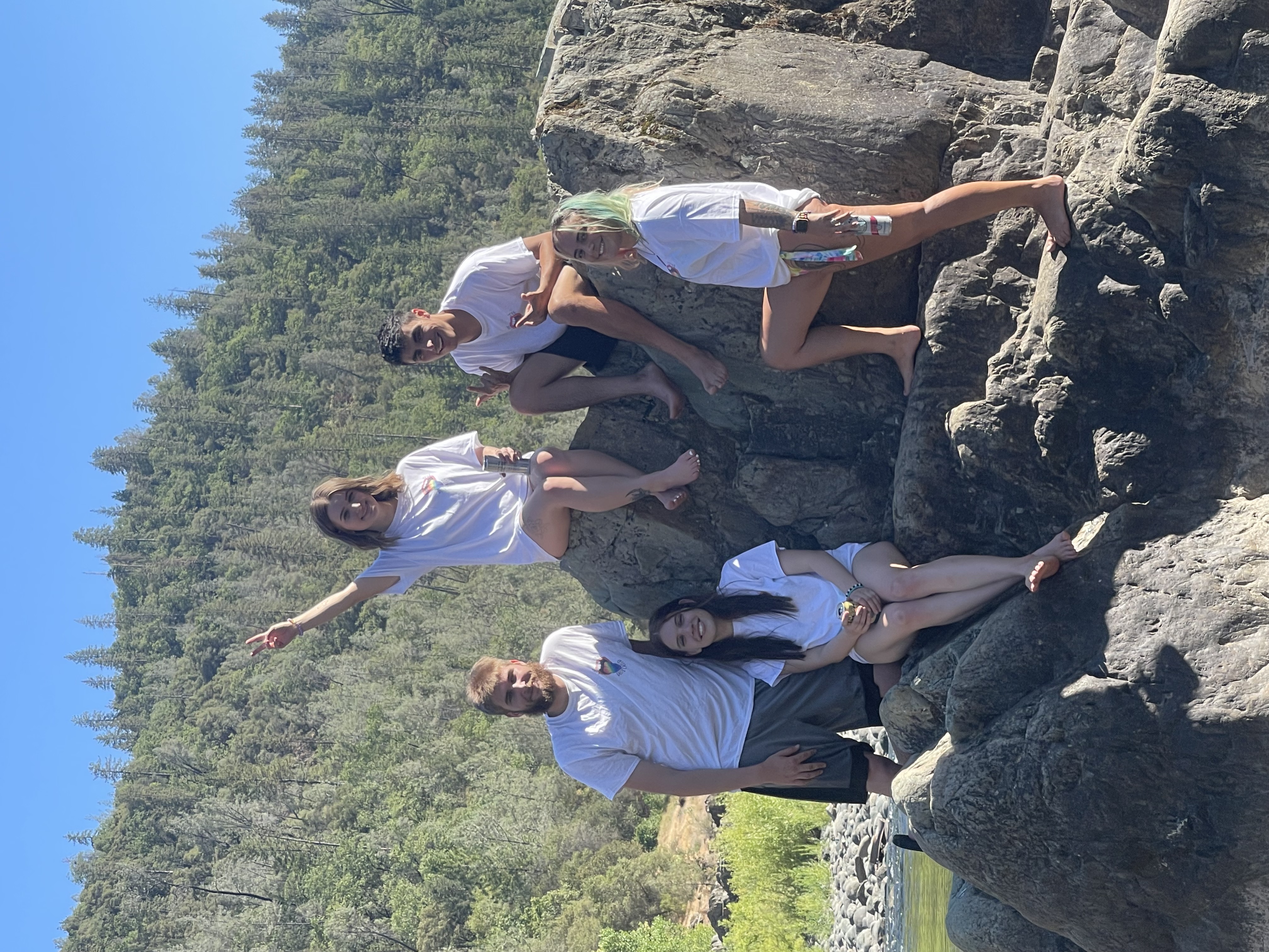 A group picture of me and my friends on a rock with large trees and blue sky in the background