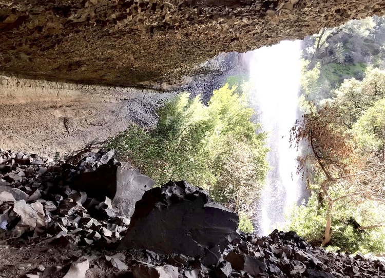 Inside a cave crevice with a waterfall pouring from above, right next to it