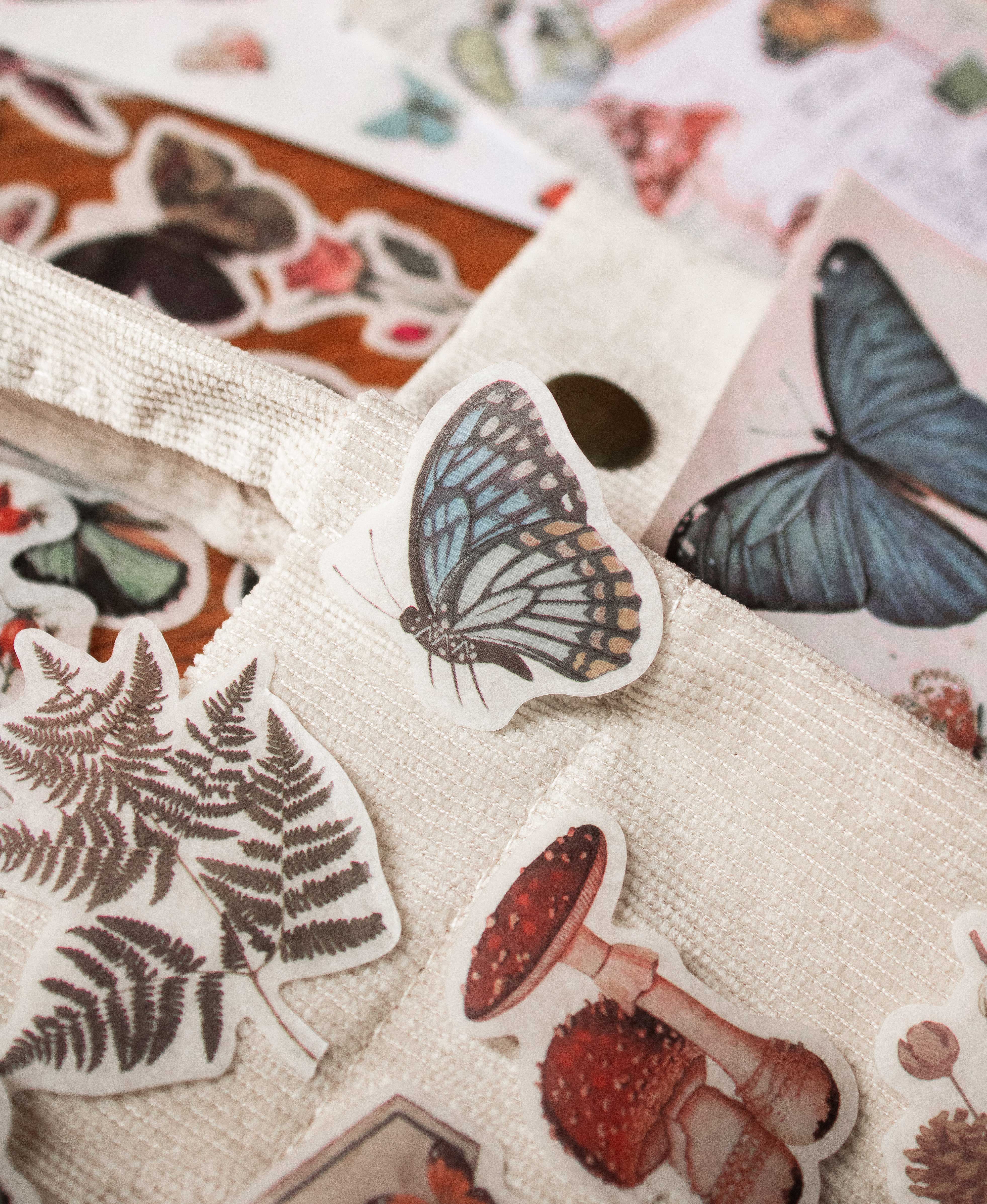 Printed stickers of drawings of butterflies, mushroom, leaves laid out on a cloth.