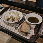 A plate of borshch and a plate of pierogi with two slices of bread on the side.