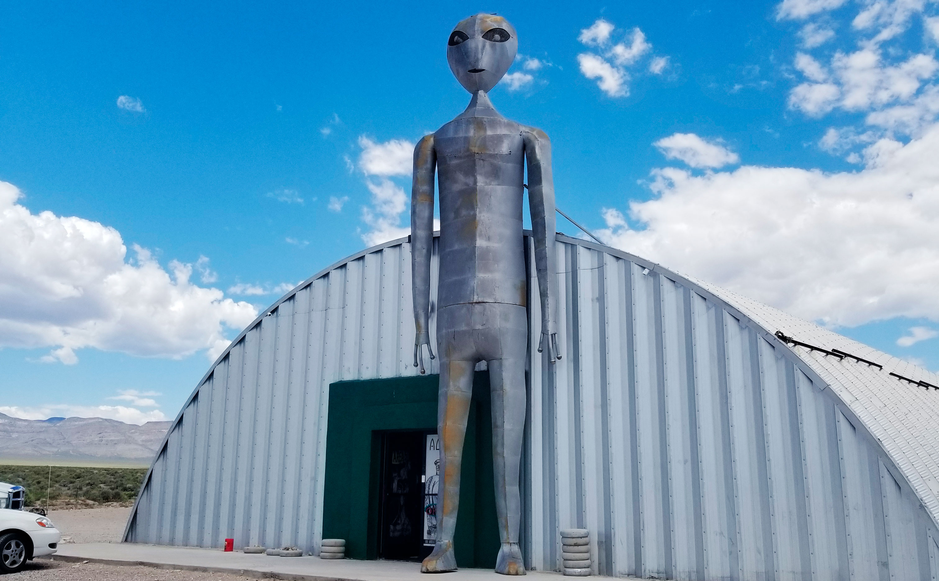 Image of large metal Alien in front of a building in the desert.