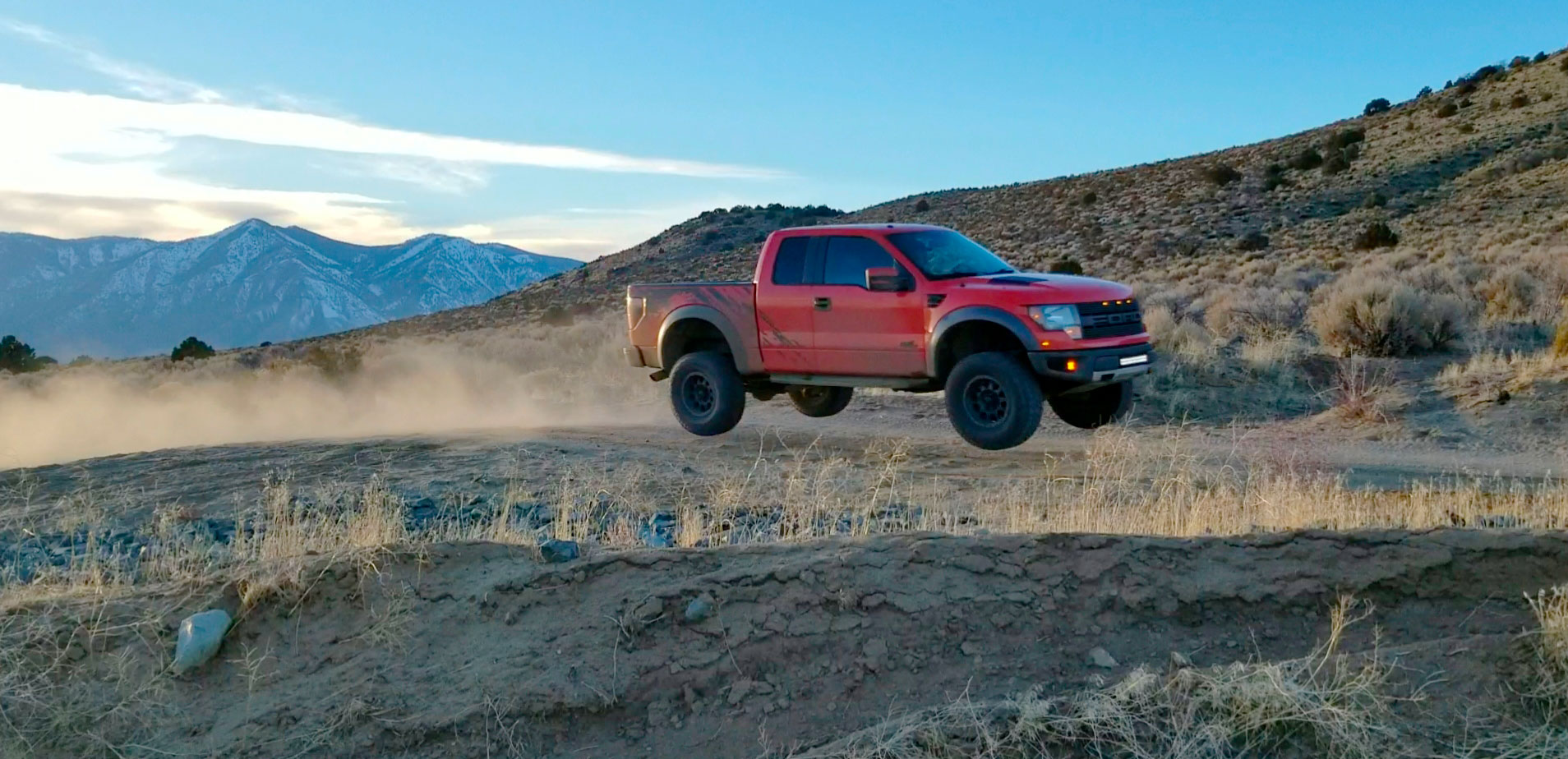 Image of Orange Ford Raptor truck jumping in the desert.