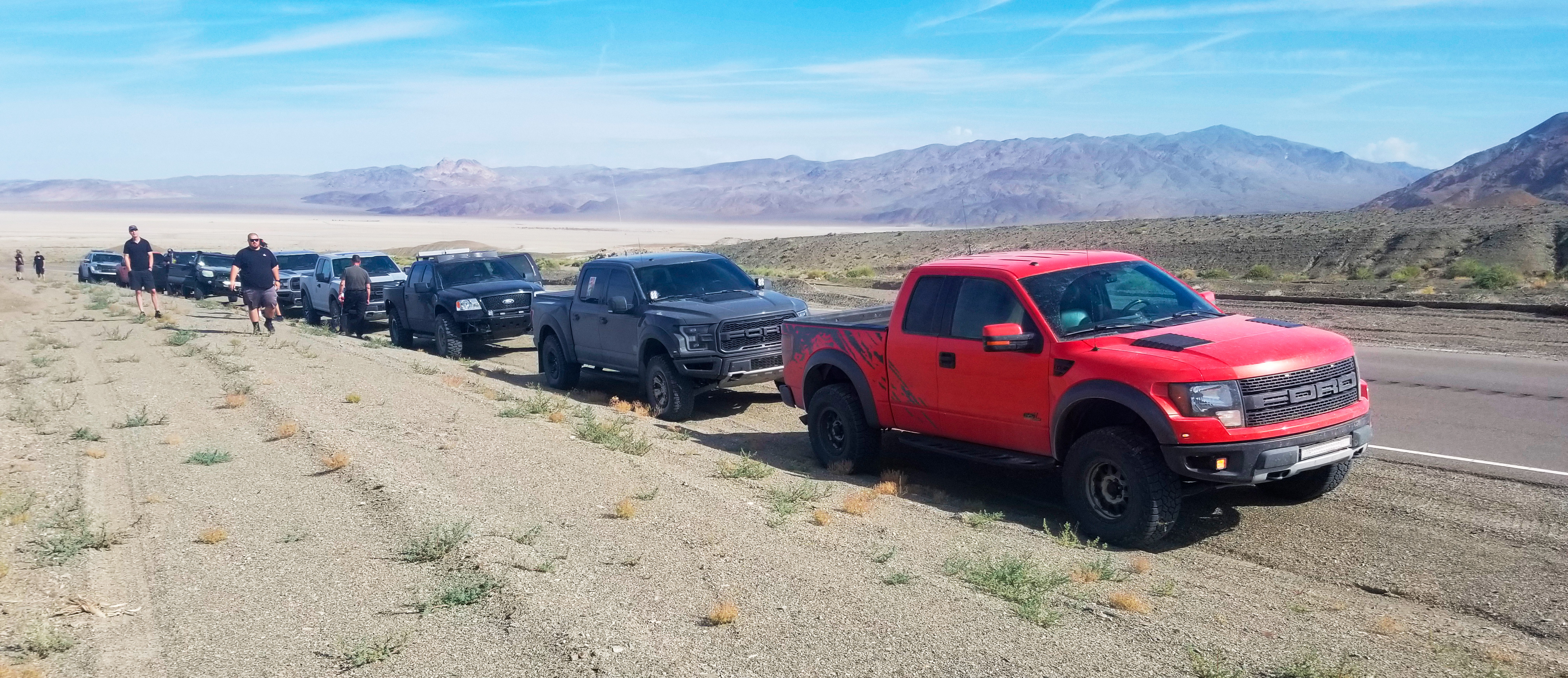 Image of multiple Ford Raptor trucks in the desert with mountain range in the background.