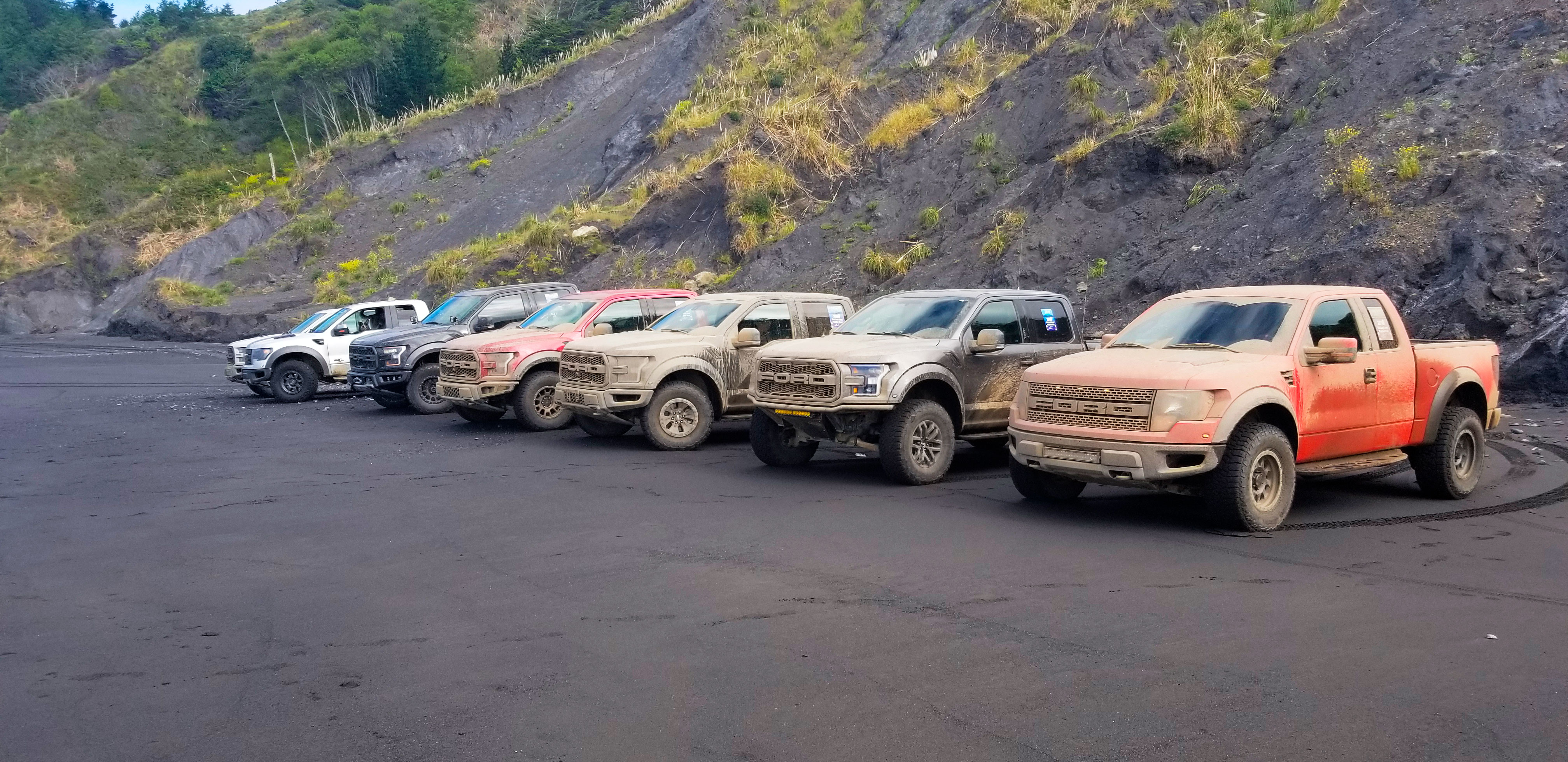 Image of multiple Ford Raptor trucks on a black sand beach.