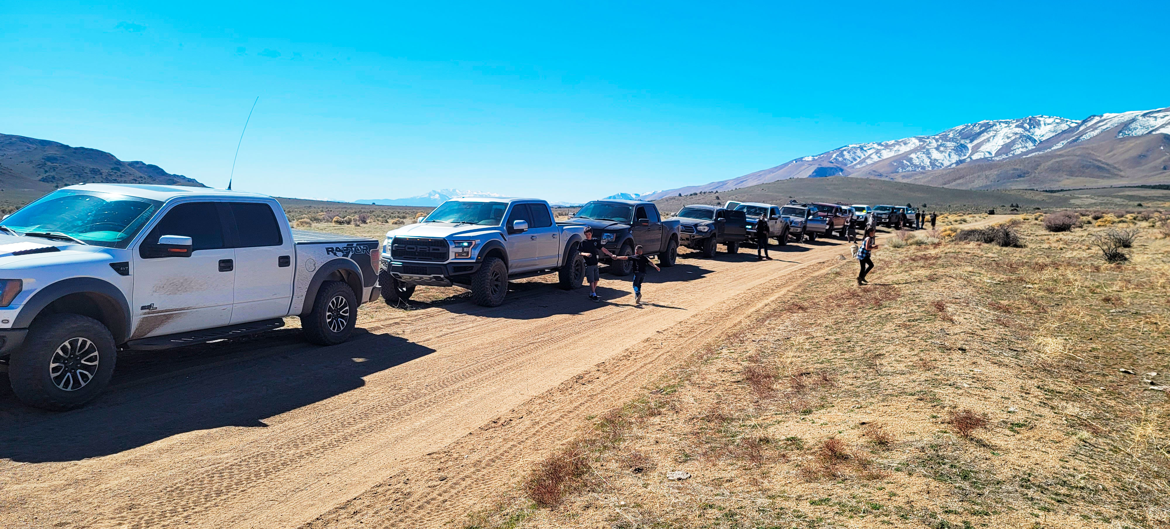 Image of multiple Ford Raptor trucks in the desert with snow cap mountains in the background.