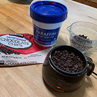 Chocolate candy melter, chocolate chips and paraffin on a counter top.