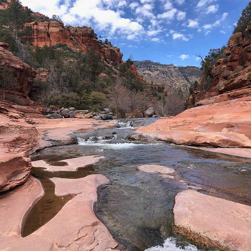 Smooth rocks line the river with red and brown layered desert mountains in the background