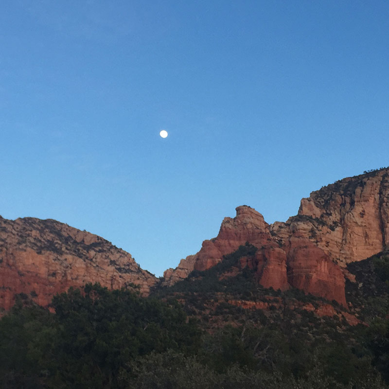 The brown and red layered mountains of the desert with a full moon above