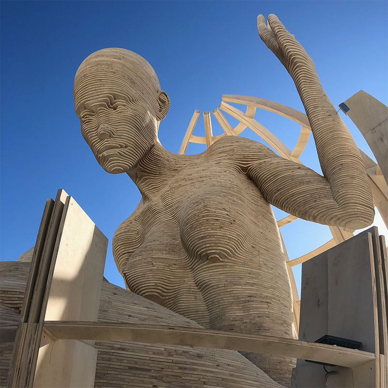 A layered wooden statue of a nude woman reading a book