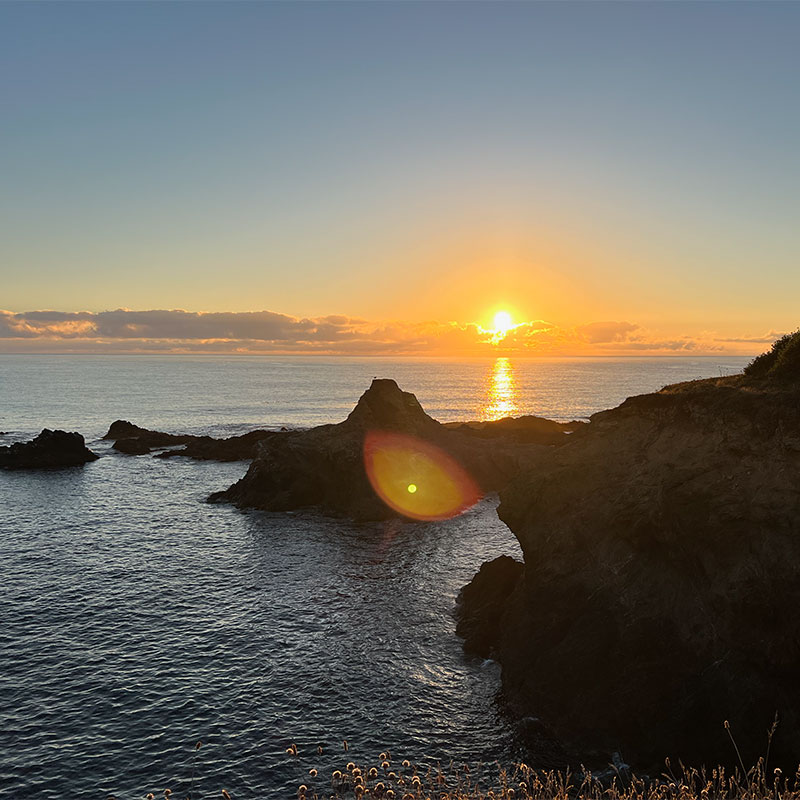 The yellow sun falls behind the clouds over a rocky ocean