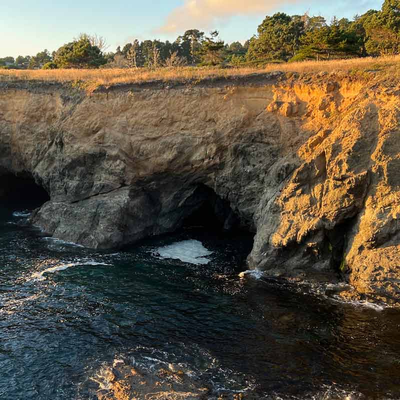 The waves break on a small ocean cave beneath a cliff