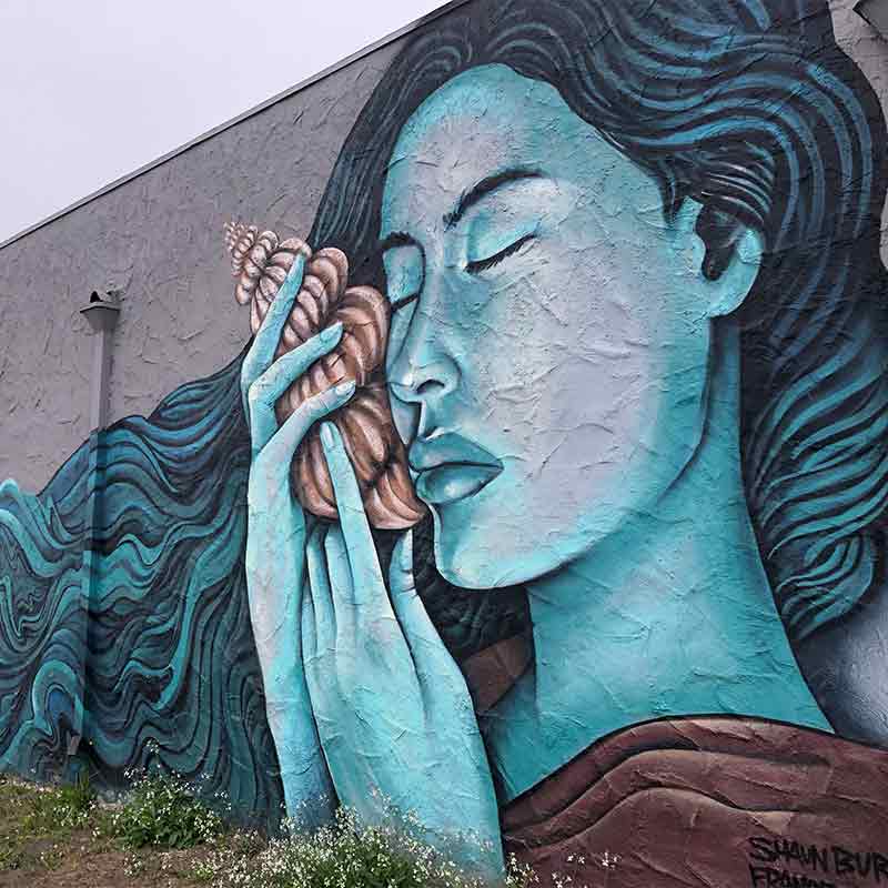 A mural of a blue-skinned woman holding a seashell to her ear