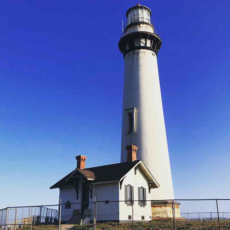 A white lighthouse tower stabds tall over a deep blue sky