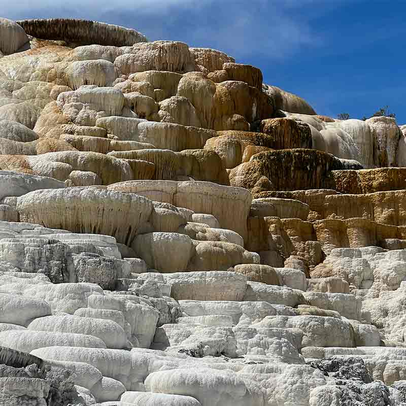 A brown and white layered hot spring trickels down with warm water against a blue sky