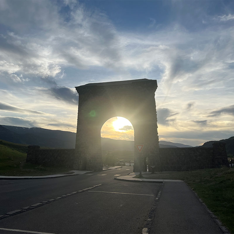 An entrance gate to yellowstone at sunset with the sun peaking through the gate