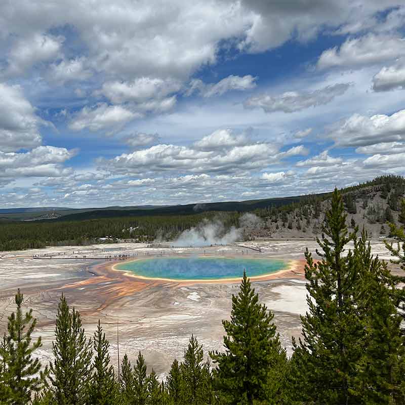 An image of the grand prismatic spring with a deep blue pool of rainbow colors seen from above with a cloudy sky
