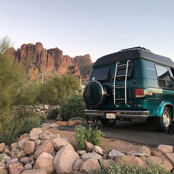 A green van backed into a camping spot surrounded by rocks and a rocky mountain in the background