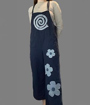A model wearing blue overalls with a denim patch shaped like a swirl on the chest and three denim patches shaped like flowers on the leg