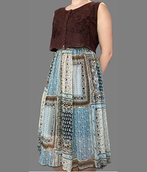 A model weaing a cropped, dark brown, button up tank top and a blue and brown patterned, flowy, ankle length, skirt.