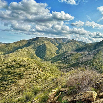 Pathway view of green valley mountains under a beautiful blue sky with fluffy clouds.