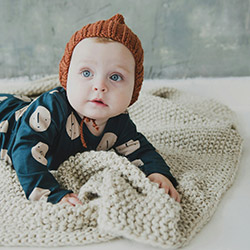 Baby facing the camera laying down on top of a crochet blanket