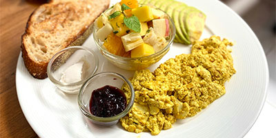 A plate with scrambled tofu and a cup of fruit.