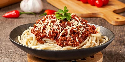 A bowl of spaghetti with various ingredients in the background.