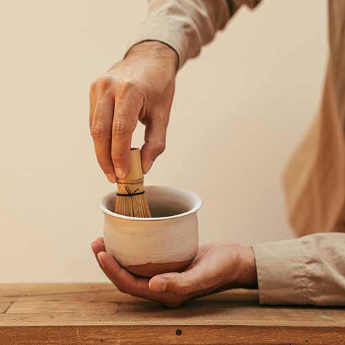 One hand holding a clay bowl while the other hand is whisking in the bowl.