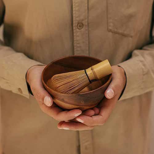 hands holding a wooden bowl with a whisk inside.