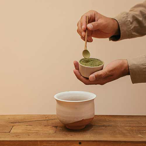 Hands scooping out matcha powder from a container.