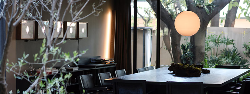 A picture of inside a beautiful resturant, it has a big black table, a light fixture, and plants