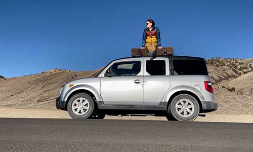 woman sitting on top of vehicle parked in the desert