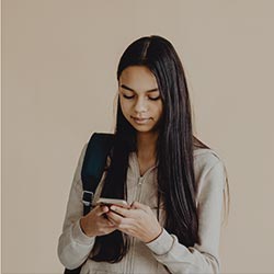 A girl in beige clothing stares at her phone.