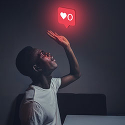 A man in the dark looking up at a hovering red like button.