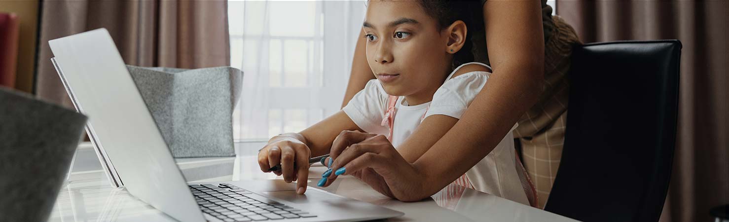 An adult and child are together on the same laptop.