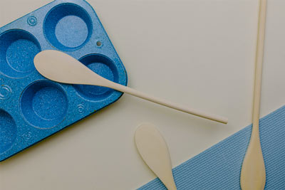 A blue muffin pan next to three wooden mixing spoons on a beige background.