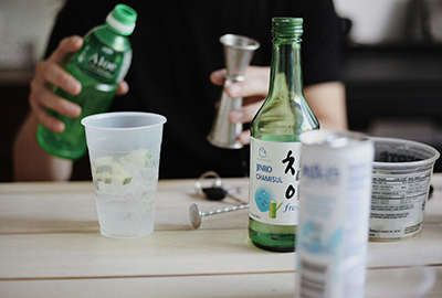 Someone pouring soju into a shot glass with a bottle of Jinro nearby