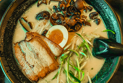Creamy tonkotsu ramen with soft-boiled egg, pork belly, mushrooms and green sprouts in a black bowl