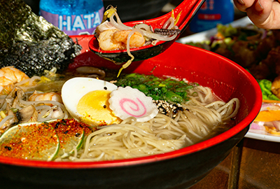Seafood ramen with boiled egg, lime, narutomaki and vegetables served in red bowl with Japanese drinks on the side