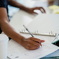A person at an office desk making a draft on paper with a pen. 