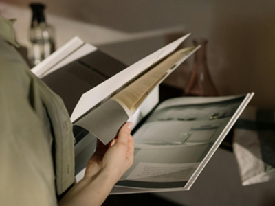 A person flipping through a magazine, the light from the outside reflecting onto the pages.