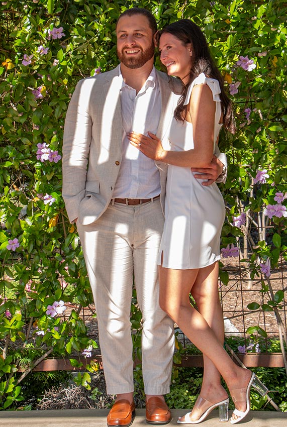 Photo of a couple standing next to each other with greenery in the background