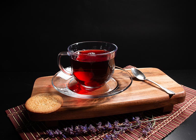 Photo of some tea in a clear cup and plate sitting on a cutting board with a round cookie next to it